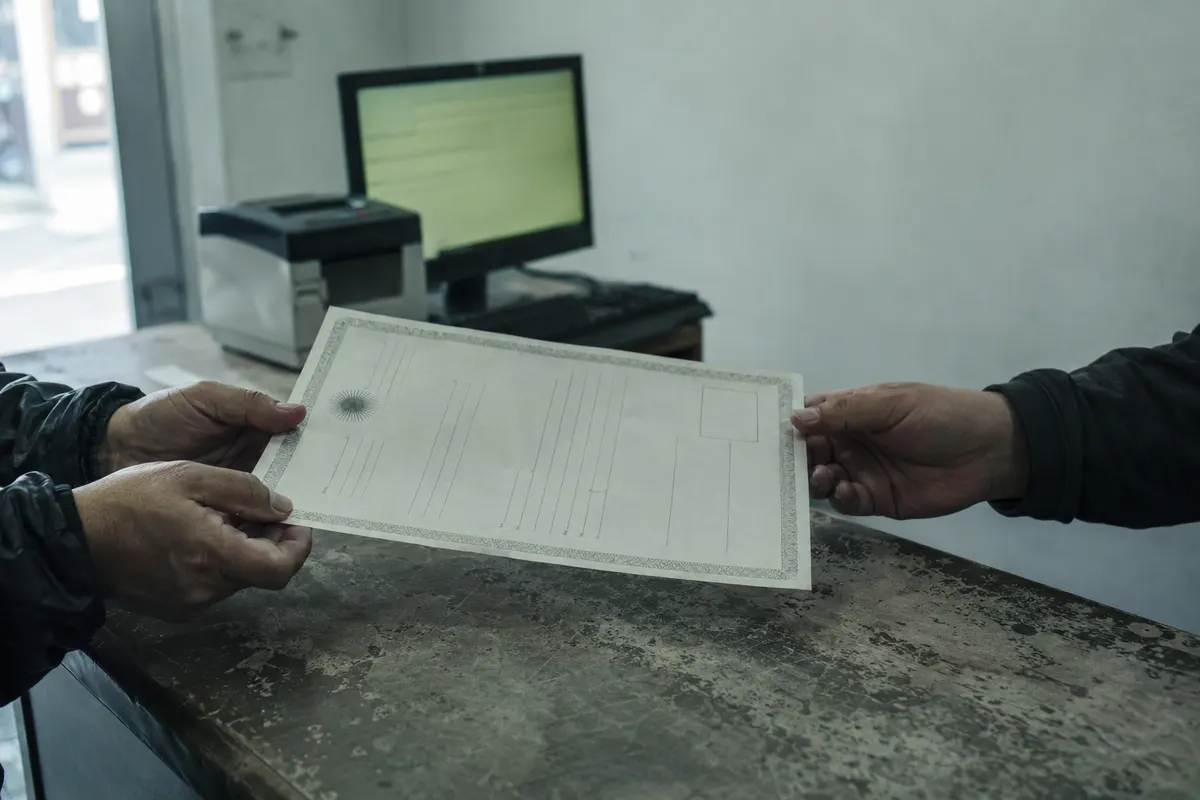 Dos manos intercambian sobre el mostrador un comprobante impreso con formato oficial, mientras al fondo esperan la computadora de facturación y la impresora del negocio